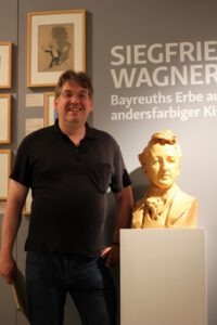 Thorsten Scharnke an der Siegfried Wagner-Büste von Adolf von Hildebrand in der Ausstellung im Schwulen Museum Berlin